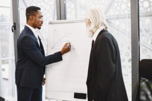 Two business leaders review a hand-drawn chart on a flip board during a strategy discussion.